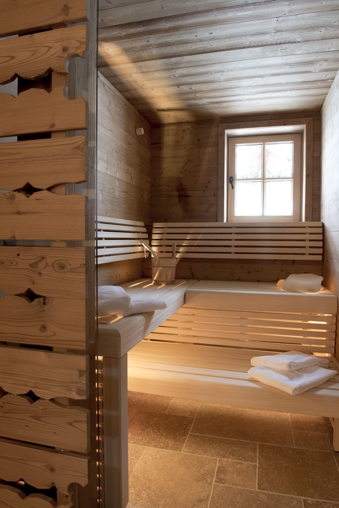 Gemütliche Sauna in der Lech Lodge, ausgekleidet mit der alpinen Wandpaneele „Gran Paradiso“. Die natürliche Holzoptik schafft eine warme, entspannende Atmosphäre, unterstrichen durch indirekte Beleuchtung und traditionelles Design.