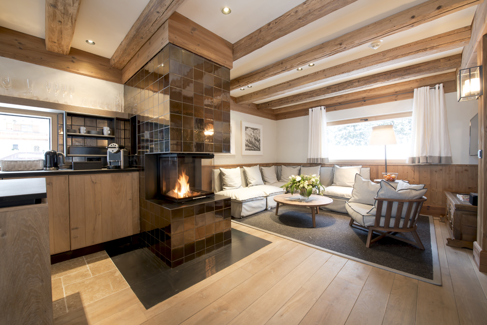 Elegantes Wohnzimmer in der Lech Lodge, ausgestattet mit der thermisch behandelten alpinen Wandpaneele „Gran Paradiso 212°“. Kombination aus Naturholz, Sichtbalken und modernem Kamin schafft exklusives alpines Wohnambiente.