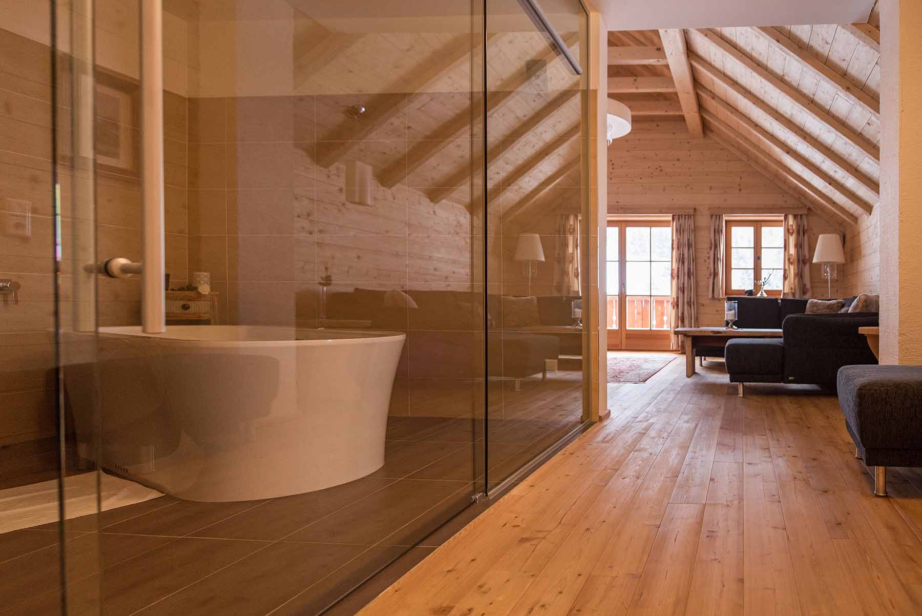 Gemütlicher Wohnbereich mit sichtbarer Dachschräge und freistehender Badewanne hinter Glas. Wandverkleidung aus gehackten Alpine Wandpaneelen Großglockner im Bergdorf Donnersbachwald.