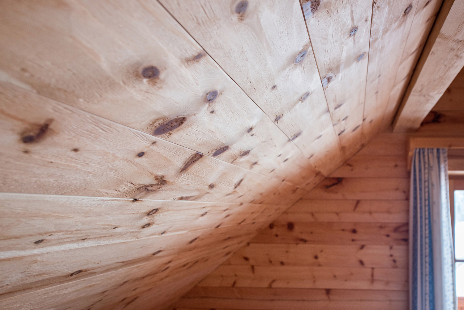 Detailaufnahme einer Dachschräge mit Alpine Wandpaneelen Piz Palü im Bergdorf Donnersbachwald, naturbelassene Holzoberfläche mit markanter Maserung und Ästen.