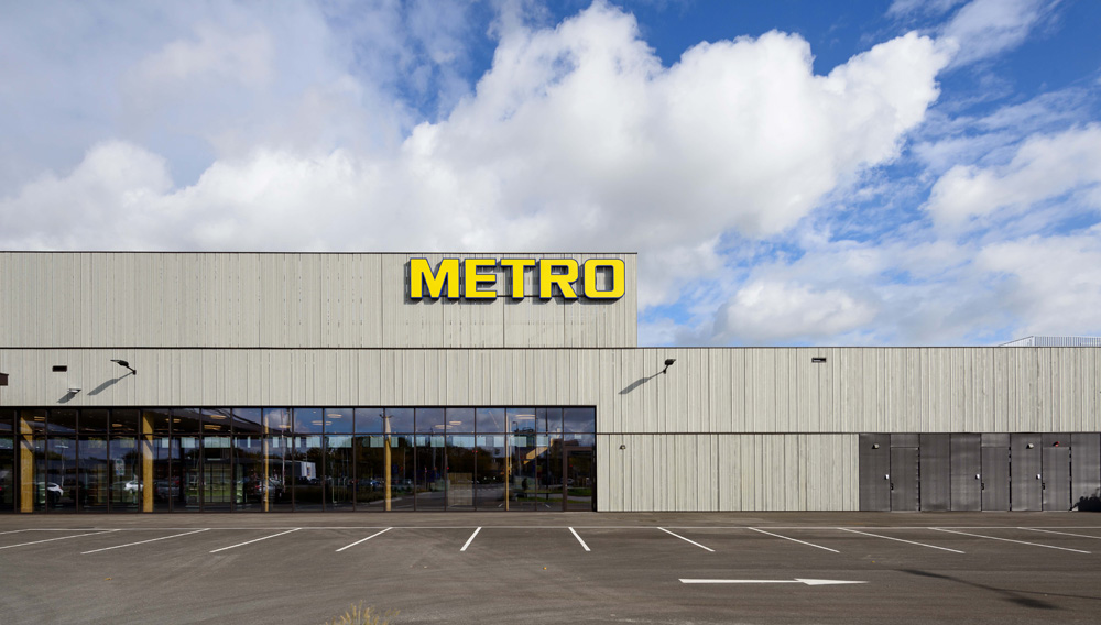 Frontansicht des METRO-Markts in St. Pölten mit großem gelbem Logo und Fassade aus vertikal verbauter, vorvergrauter Thermofichte unter bewölktem Himmel.