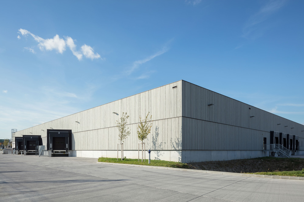 Großes METRO-Lagergebäude in St. Pölten mit moderner vorvergrauter Thermofichte-Fassade, Laderampen und junger Bepflanzung unter blauem Himmel.