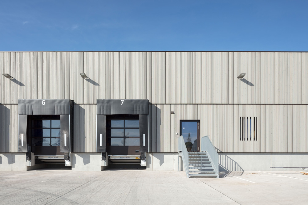 Ladebereich der METRO St. Pölten mit senkrechter Holzfassade aus vorvergrauter Thermofichte, zwei Laderampen, eine Metalltreppe und klarer Himmel im Hintergrund.