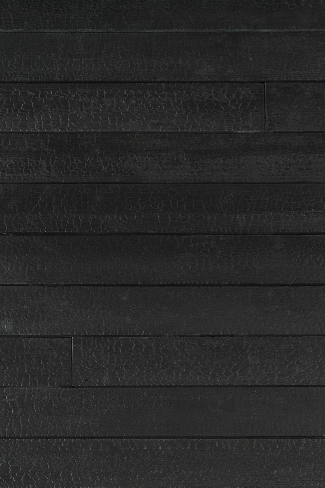 Nahaufnahme der Alpine Wandpaneele Vulcano in verkohlter Optik. Die dunklen Holzoberflächen mit charakteristischer Struktur und Textur zeigen die markante, durch Hitze behandelte Oberfläche mit feinen Rissen und Farbnuancen.
