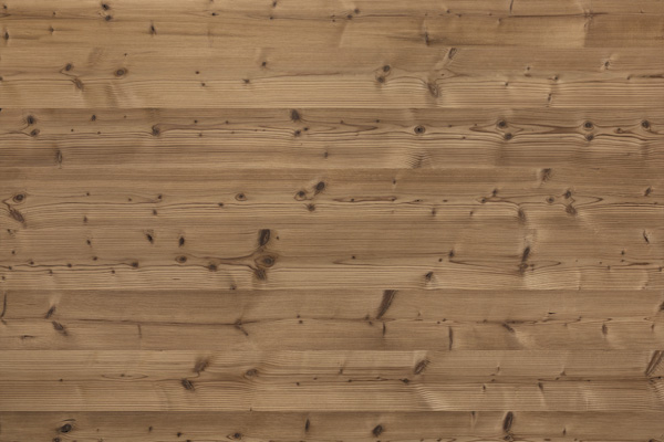 Nahaufnahme einer gebürsteten Holzoberfläche des Typs "Gran Paradiso 212" von Mareiner Holz. Die strukturierte Maserung und die natürlichen Astlöcher sind gleichmäßig über das mittelbraune, seidenmatt wirkende Holz verteilt, was dem Material eine warme und lebendige Anmutung verleiht.