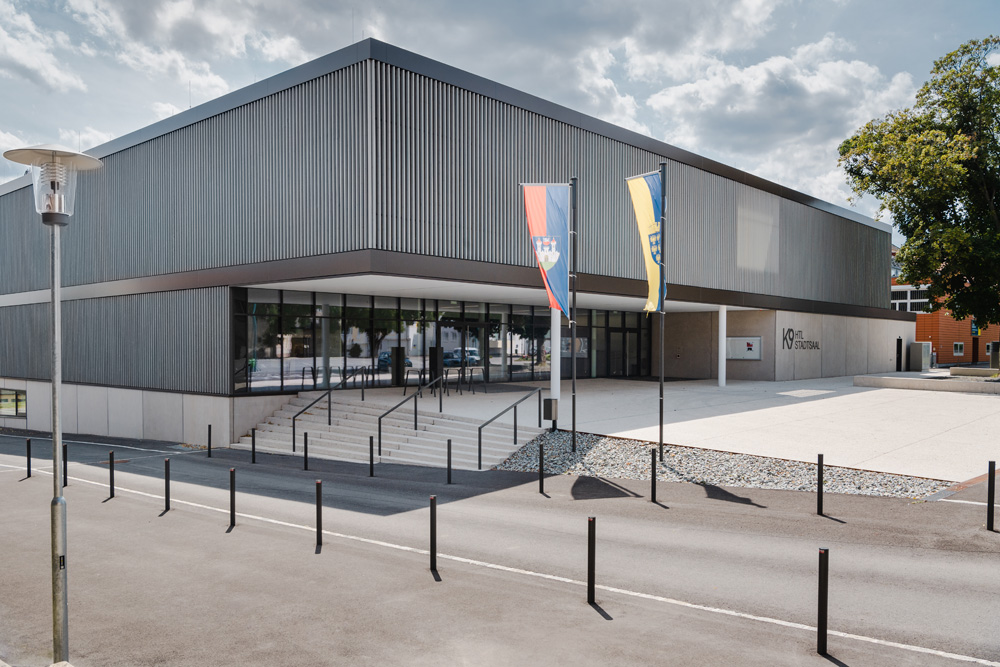 Moderne Schulfassade der HTL Zistersdorf mit vertikaler Verkleidung aus vorvergrauter Thermofichte; klare Linien, große Fensterflächen und repräsentativer Eingangsbereich mit Fahnen und breiter Treppe.