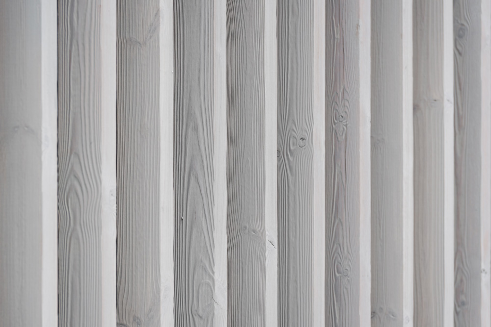 Nahaufnahme vertikaler Fassadenlamellen aus vorvergrauter Thermofichte mit sichtbarer Holzmaserung und feiner Struktur.