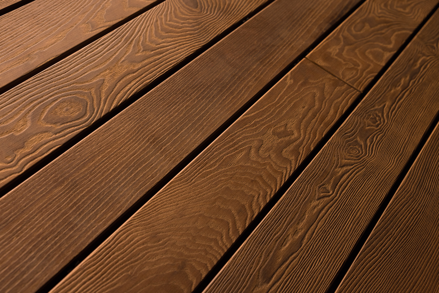 Terrassendielen mit gebürsteter Oberfläche in einem warmen Dunkelbraun. Die ausgeprägte Maserung ist deutlich spürbar und verleiht den Dielen eine lebendige, strukturierte Haptik mit natürlichem, rustikalem Charakter.