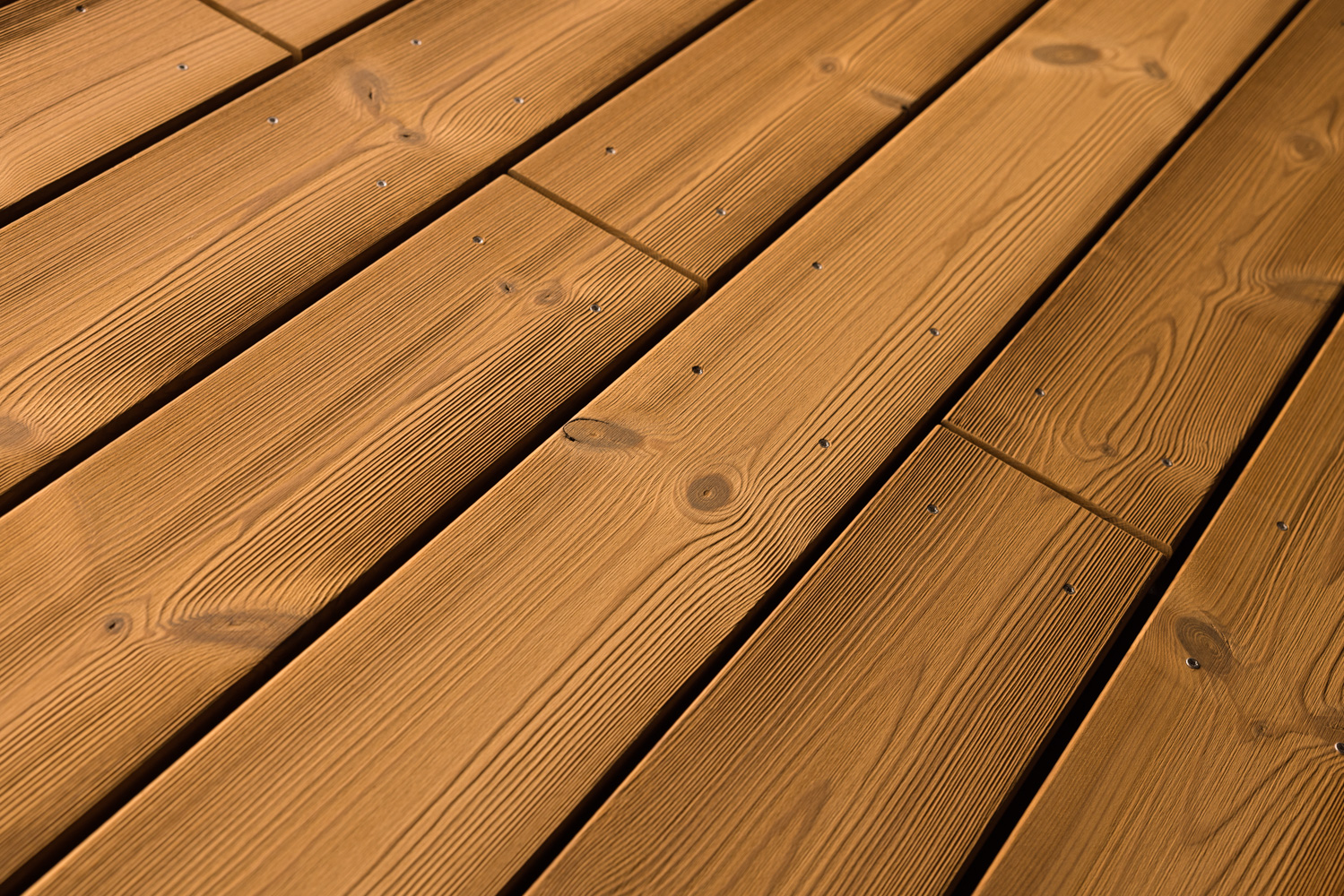 Terrassendielen mit gebürsteter Oberfläche in warmem Braunton. Die feine Maserung und natürliche Aststrukturen sind betont sichtbar, kleine Schraubenköpfe sorgen für eine präzise, funktionale Optik mit handwerklichem Charakter.