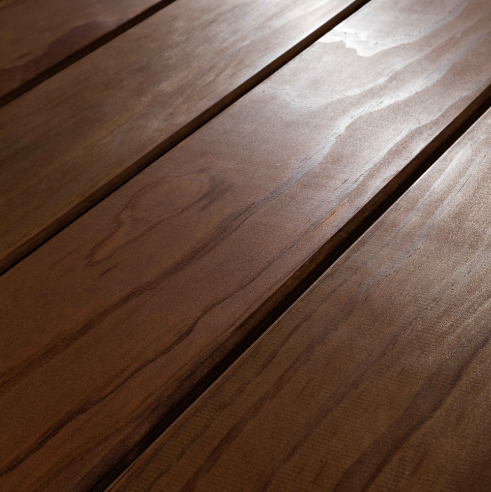 Makroaufnahme der Holzterrassendiele Kebony mit glatter Oberfläche und eleganter, leicht rötlich-brauner Tönung. Die Maserung ist sanft fließend, ohne starke Rillen, was eine moderne und zugleich natürliche Wirkung erzeugt. Besonders langlebig und pflegeleicht – ideal für stilvolle Außenbereiche.