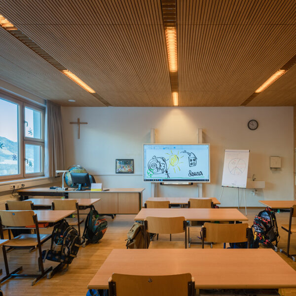 Classroom with large window front, solid wood ceiling and walls. The warm wood design promotes a healthy learning atmosphere. Modern technology such as a digital whiteboard ideally complements the natural furnishings.