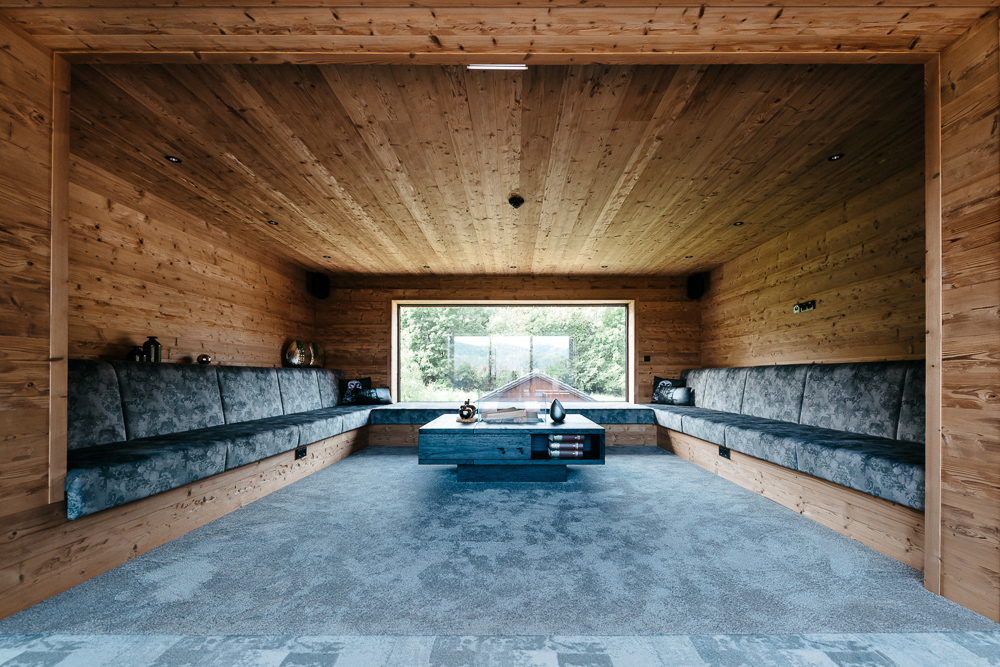 Modern gestalteter Loungebereich im Hotel Essigmanngut in Salzburg mit vollständig in Mareiner Mont Blanc Alpine Wandpaneelen verkleideten Wänden und Decken. Die U-förmige Sitzbank ist mit blaugrauen Polstern versehen.