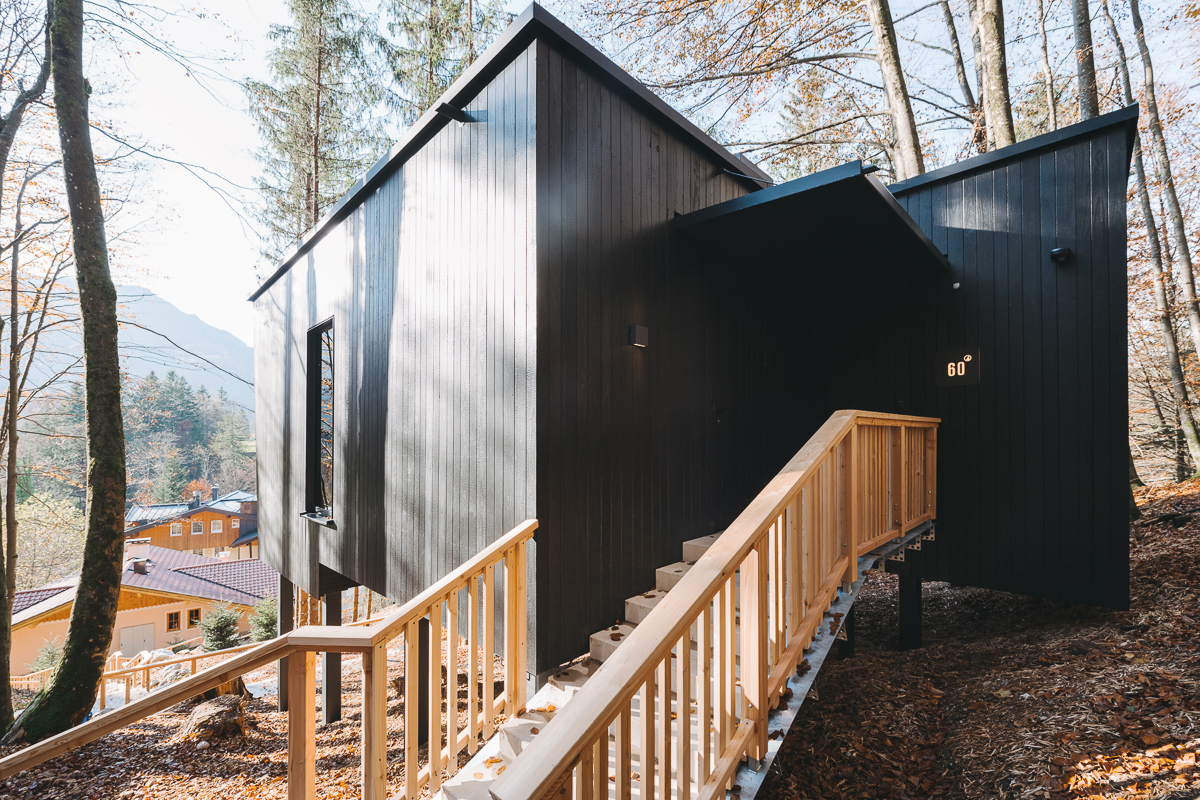 Modernes schwarzes Chalet mit verkohlter Kebony-Holzfassade und hellem Holzgeländer im Naturhotel Fischerwirt Salzburg, eingebettet in einen herbstlichen Wald.