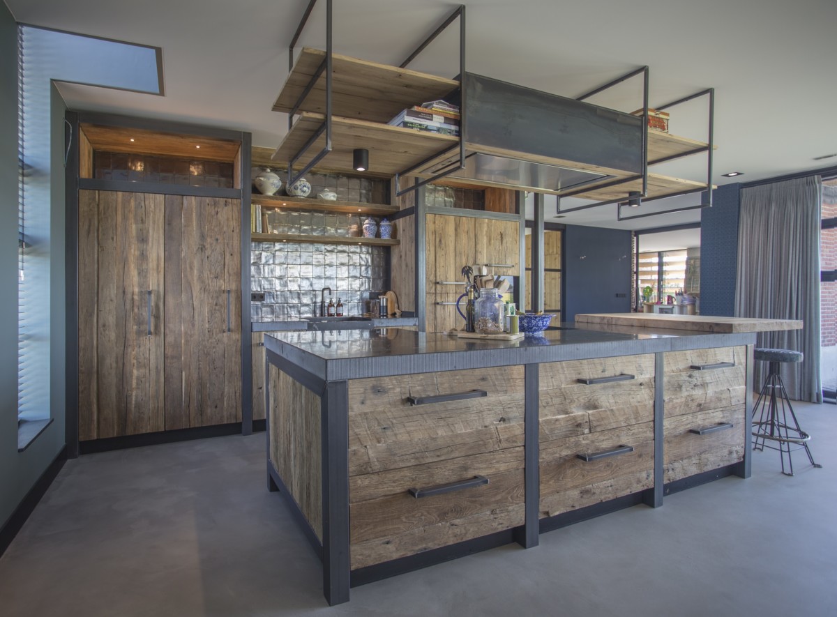 Küche mit rustikalem Charme, gefertigt aus Mareiner Altholz Sankt Moritz und Davos, kombiniert mit dunklem Stahl, modernen Geräten und einer glänzenden Arbeitsplatte.