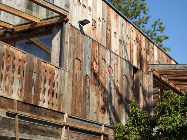 Außenfassade des Seminarzentrums der Baum aus Mareiner Altholz (Gstaad und Zermatt Gris) mit kunstvoll ausgeschnittenen Ornamenten und warmen, natürlichen Farbtönen in der Holzstruktur.