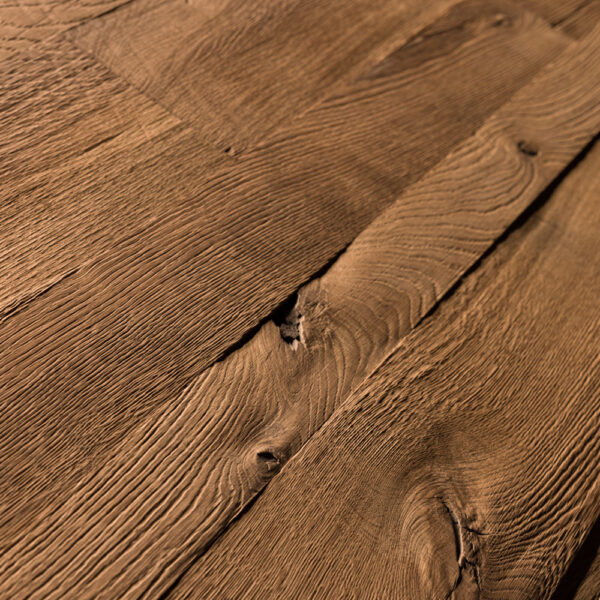 Strukturreiche Holzoberfläche mit tiefen, naturbelassenen Rillen und Astlöchern. Die rustikale Optik betont die ursprüngliche Maserung und erzeugt eine markante, handwerklich wirkende Haptik in warmem Braunton.
