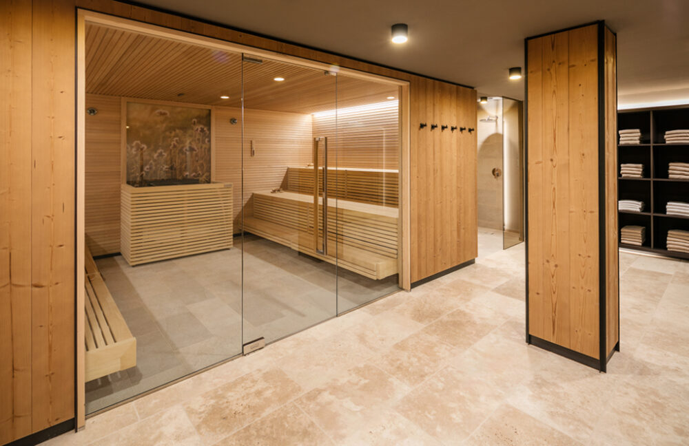 Moderner Saunabereich im Almwellness Hotel Pierer mit großzügiger Glasfront, Innenverkleidung aus hellem Holz und Wänden in Mareiner Holz Zugspitze. Ruhe und Wärme in stilvollem Wellnessambiente mit Naturmaterialien.