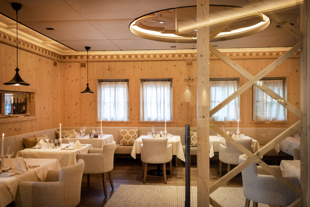 Gemütliches Restaurant mit traditioneller Einrichtung, Wandverkleidung aus hellem Mareiner Holz und elegant gedeckten Tischen. Weiche Polsterstühle und warmes Licht sorgen für eine einladende Atmosphäre.