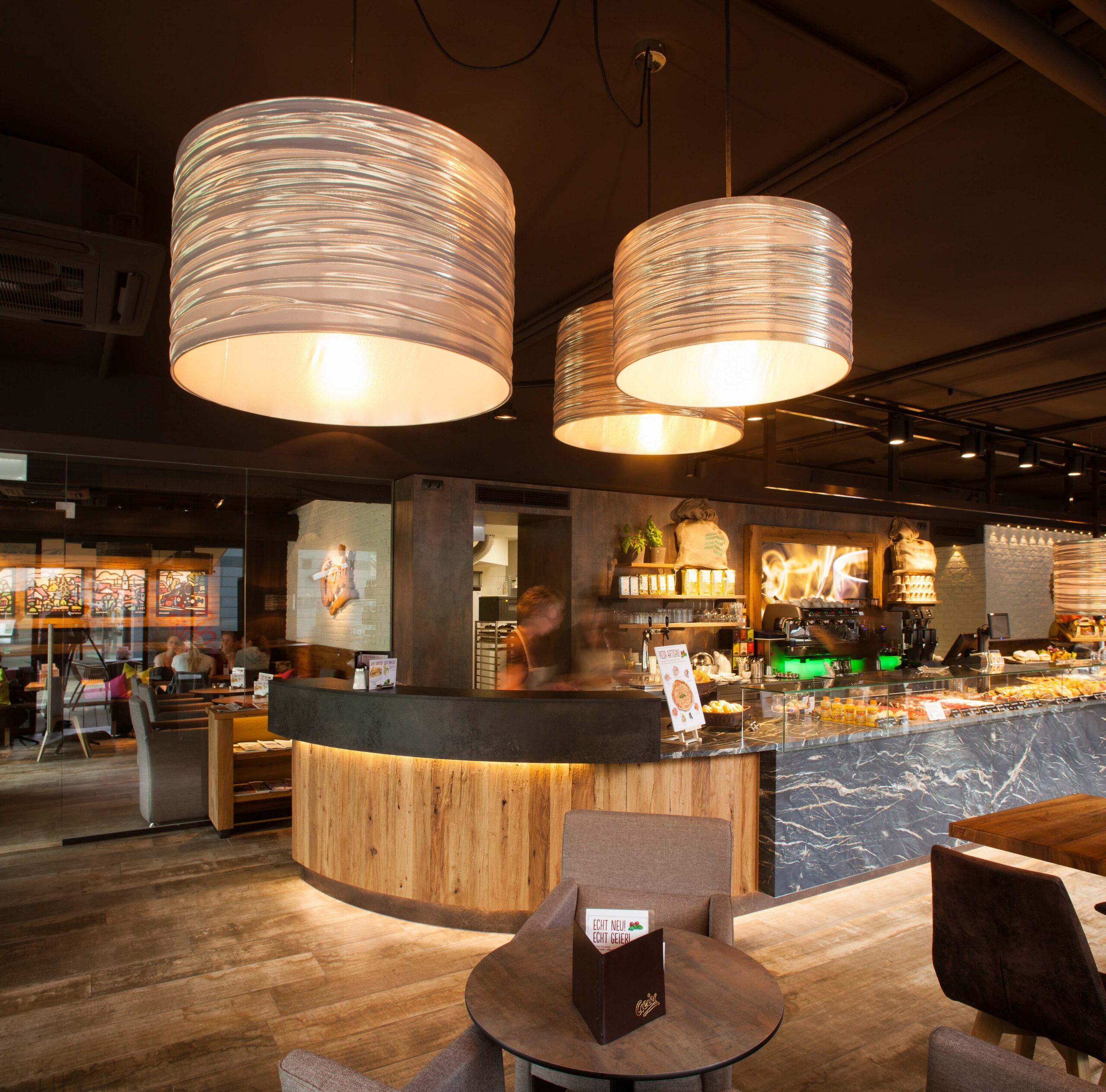 Innenraum der Bäckerei Geier mit geschwungener Theke aus Mareiner Davos Holz und stilvoller Beleuchtung – warmes, einladendes Ambiente mit natürlichen Materialien und modernem Design.