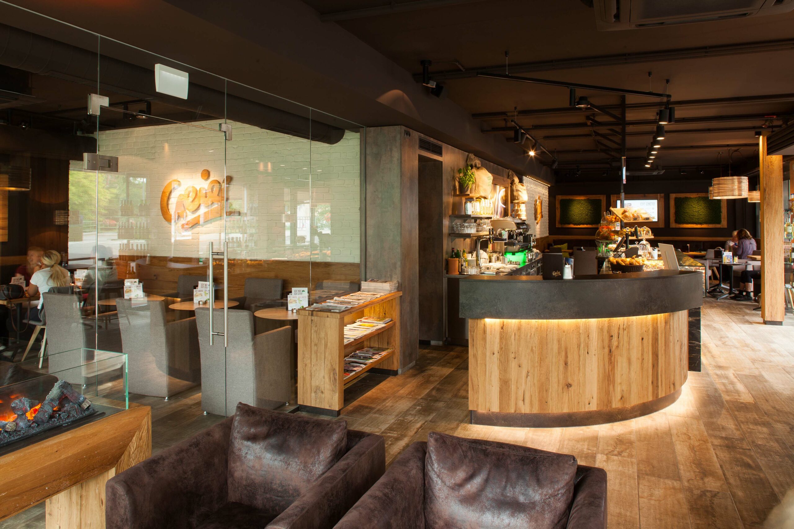 Einladendes Café-Ambiente mit Theke und Verkleidung aus Mareiner Davos Holz, gemütlicher Lounge und Sitzbereich, stilvoll beleuchtet mit moderner Ausstattung und natürlichem Design.