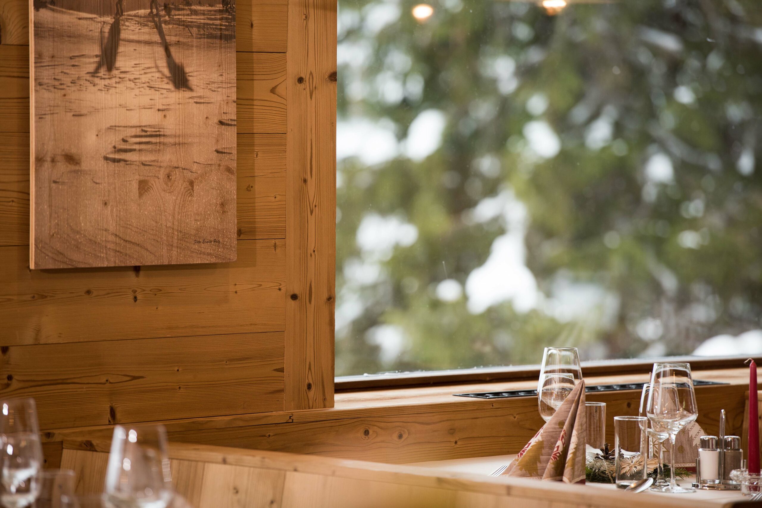 Nahaufnahme eines Fensterausschnitts mit Wandverkleidung aus Gran Paradiso 190° im Hotel Restaurant Berghof, stimmungsvoll gedeckter Tisch mit Blick ins winterliche Grün.