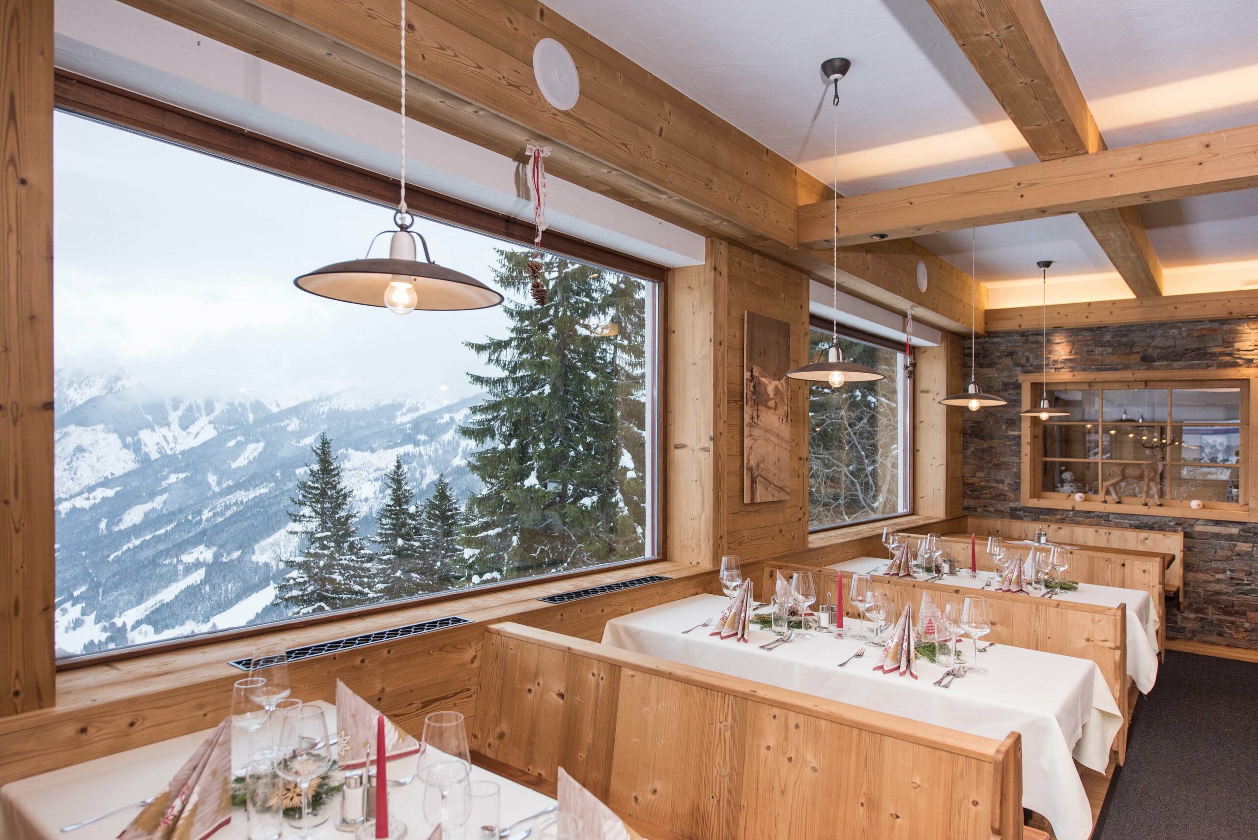 Gemütlicher Restaurantbereich mit Holzverkleidung Gran Paradiso 190°, großen Panoramafenstern und Blick auf verschneite Berglandschaft, festlich gedeckte Tische im Vordergrund.