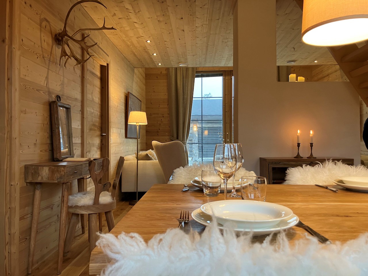 Stimmungsvoll gedeckter Holztisch im Essbereich der Lappland Chalets mit flauschigen Sitzauflagen, Kerzenlicht und gemütlicher Chalet-Atmosphäre in naturbelassener Holzverkleidung.