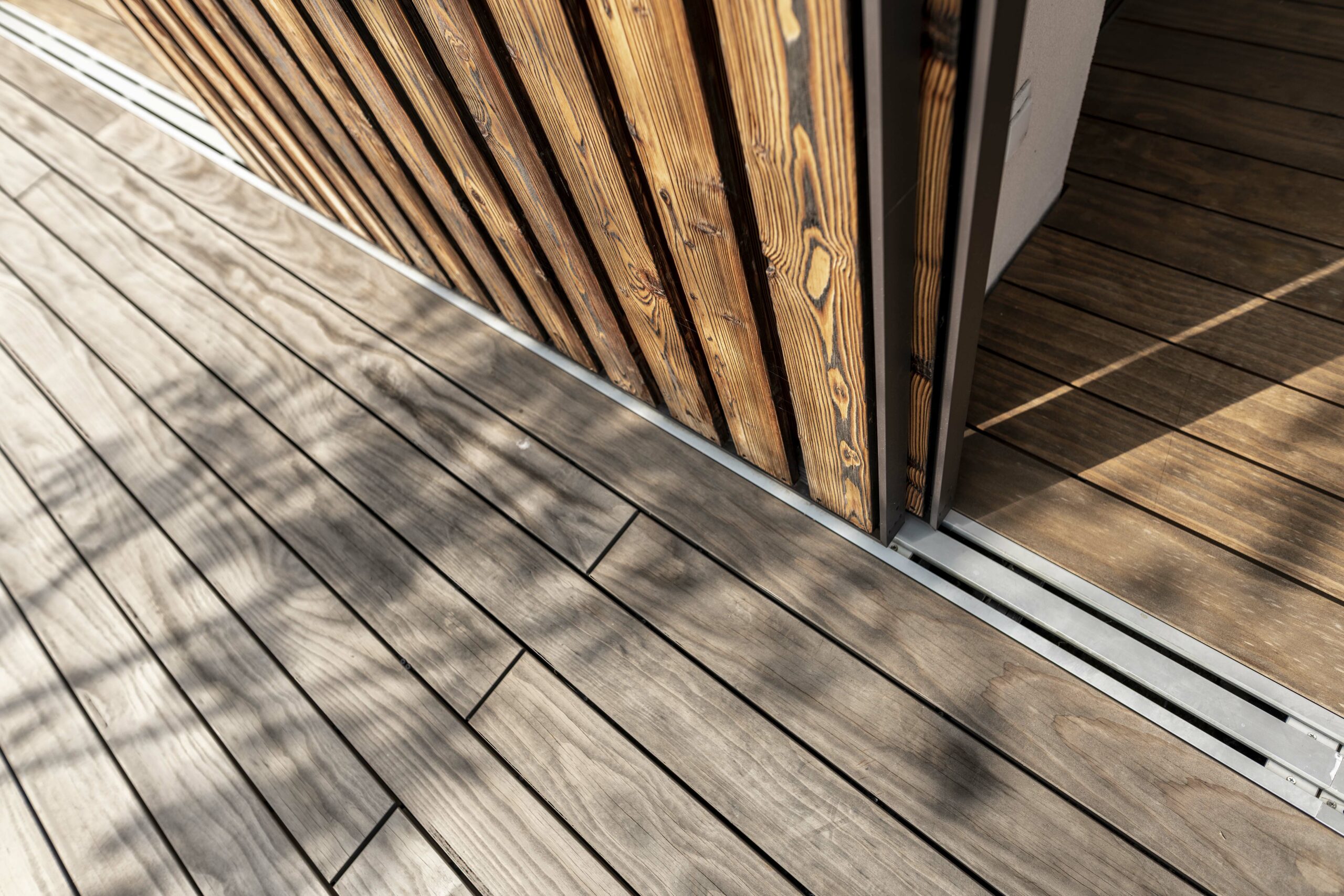 Detailaufnahme einer Terrasse aus Kebony-Holz und vertikaler Lamellenfassade aus Piz Bernina Lava – präzise Verarbeitung und natürliche Farbnuancen im harmonischen Zusammenspiel.