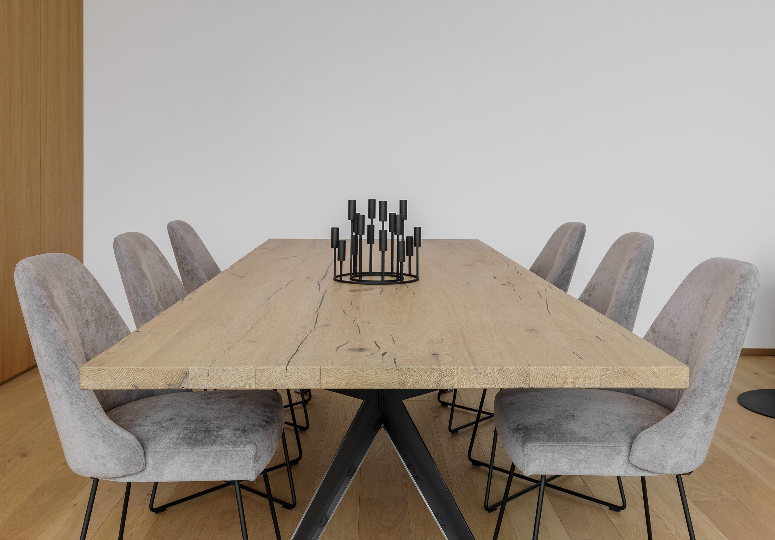 Massivholztisch Crans Montana mit natürlicher Baumkante, flankiert von sechs grauen Polsterstühlen auf schwarzem Metallgestell, auf hellem Eichenboden (Mareiner Simplon) in modernem, minimalistischem Wohnambiente.