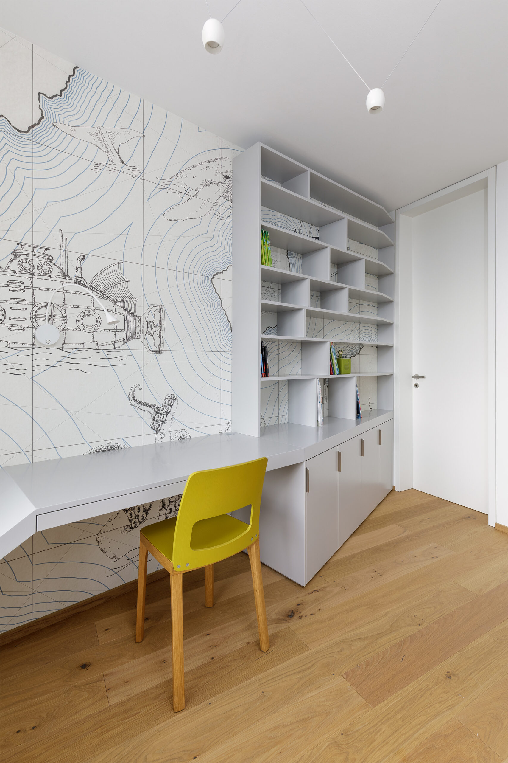 Der gezeigte Bodenbelag ist ein hochwertiger Holzboden der Produktlinie Simplon. Es handelt sich um ein naturgeöltes Eichenholz mit warmer, honigfarbener Ausstrahlung und sichtbarer Ast- und Maserstruktur, was ihm eine lebendige, authentische Wirkung verleiht. Die matte Oberfläche passt perfekt zum modernen, funktional gestalteten Interieur mit integriertem Einbauschreibtisch und Regalwand. Der Boden ergänzt die ruhige Farbpalette von Weiß und Grau und bildet einen warmen Kontrast zur minimalistischen Einrichtung.