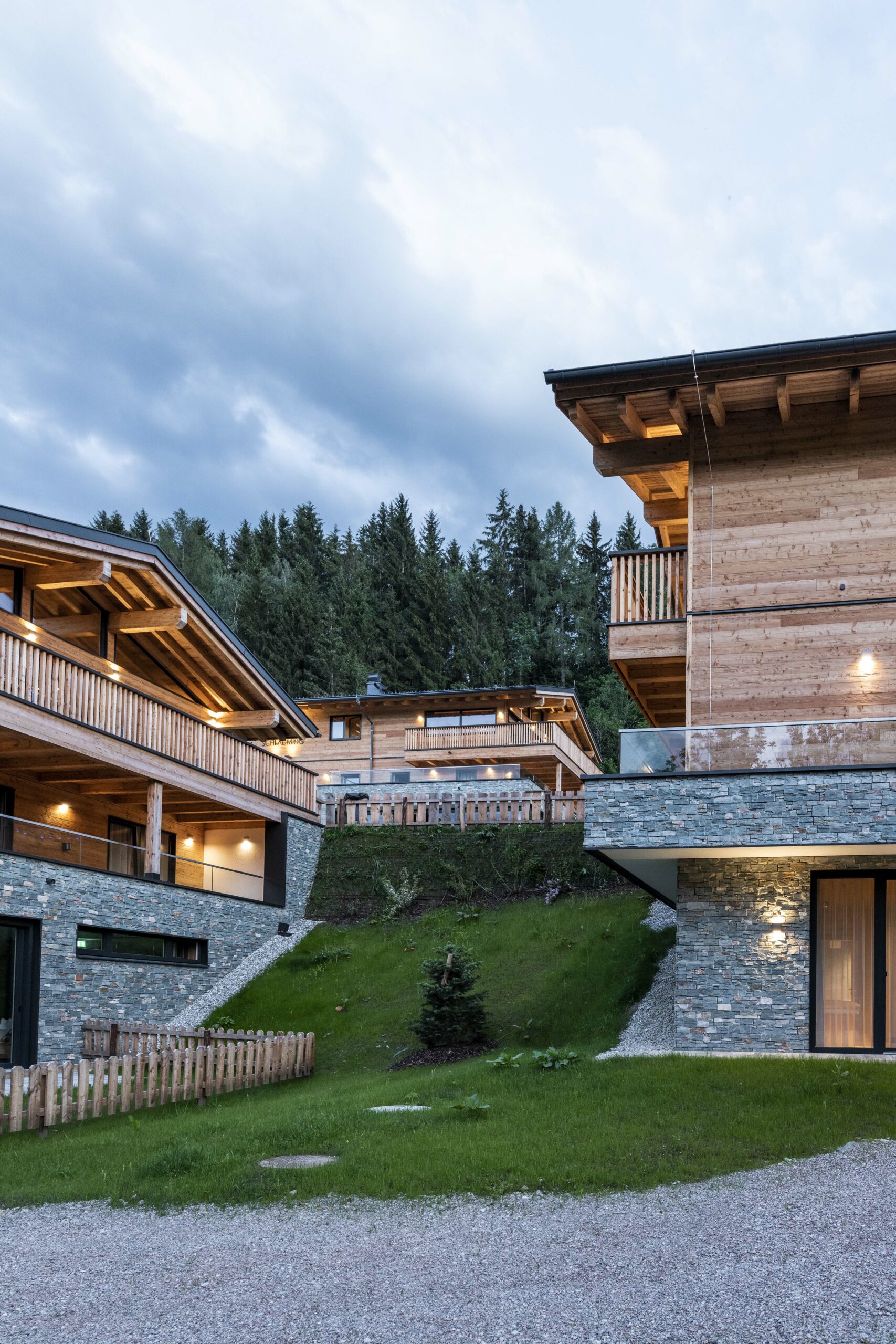 Moderne Chalets in Schladming mit charakteristischer Mareiner Piz Bernina Holzfassade und Natursteinmauern an einem begrünten Hang vor bewaldeter Kulisse.