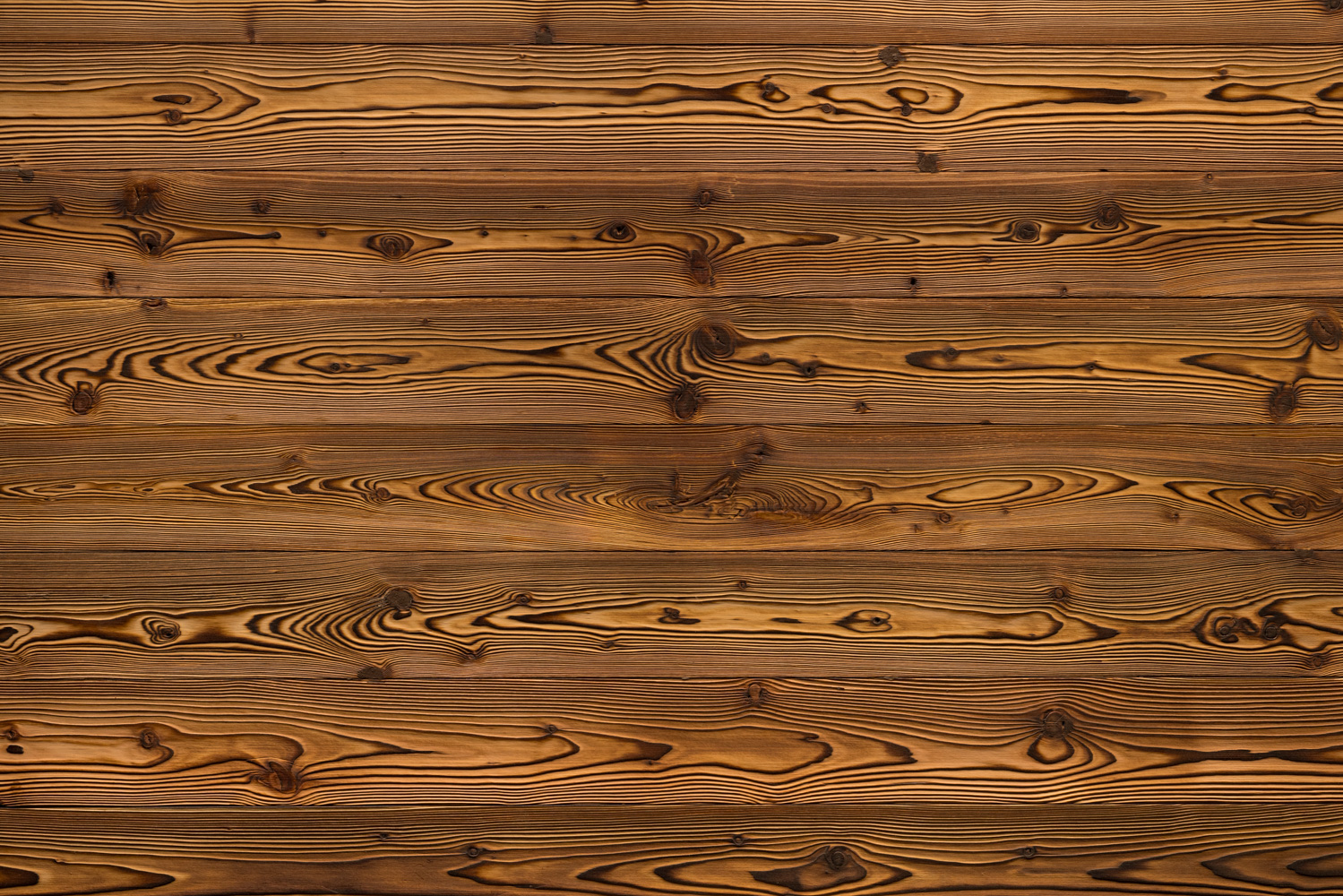 Flächige Holzoberfläche mit markanter, geflammter Optik. Die Bretter zeigen starke Kontraste zwischen hellen und dunklen Bereichen, typisch für gebranntes Holz. Ausdrucksstarke Maserung mit rustikalem Charakter für traditionelle oder moderne Akzente.