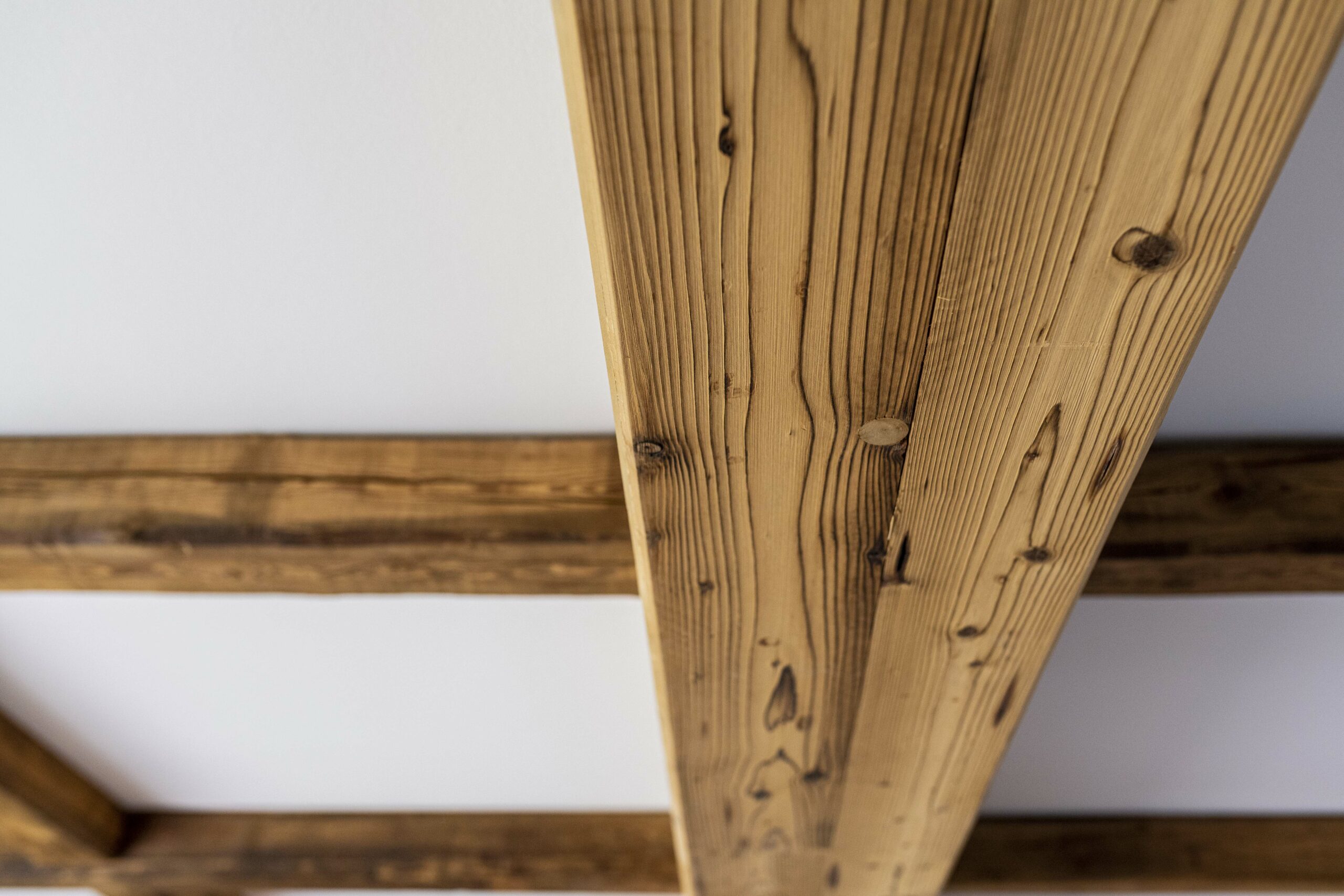 Detailansicht einer weiß verputzten Decke mit kontrastierenden Holzbalken aus Marmolada Lava. Die charakteristische Maserung und warme Tönung des Holzes verleihen dem Raum eine natürliche, rustikale Ausstrahlung.