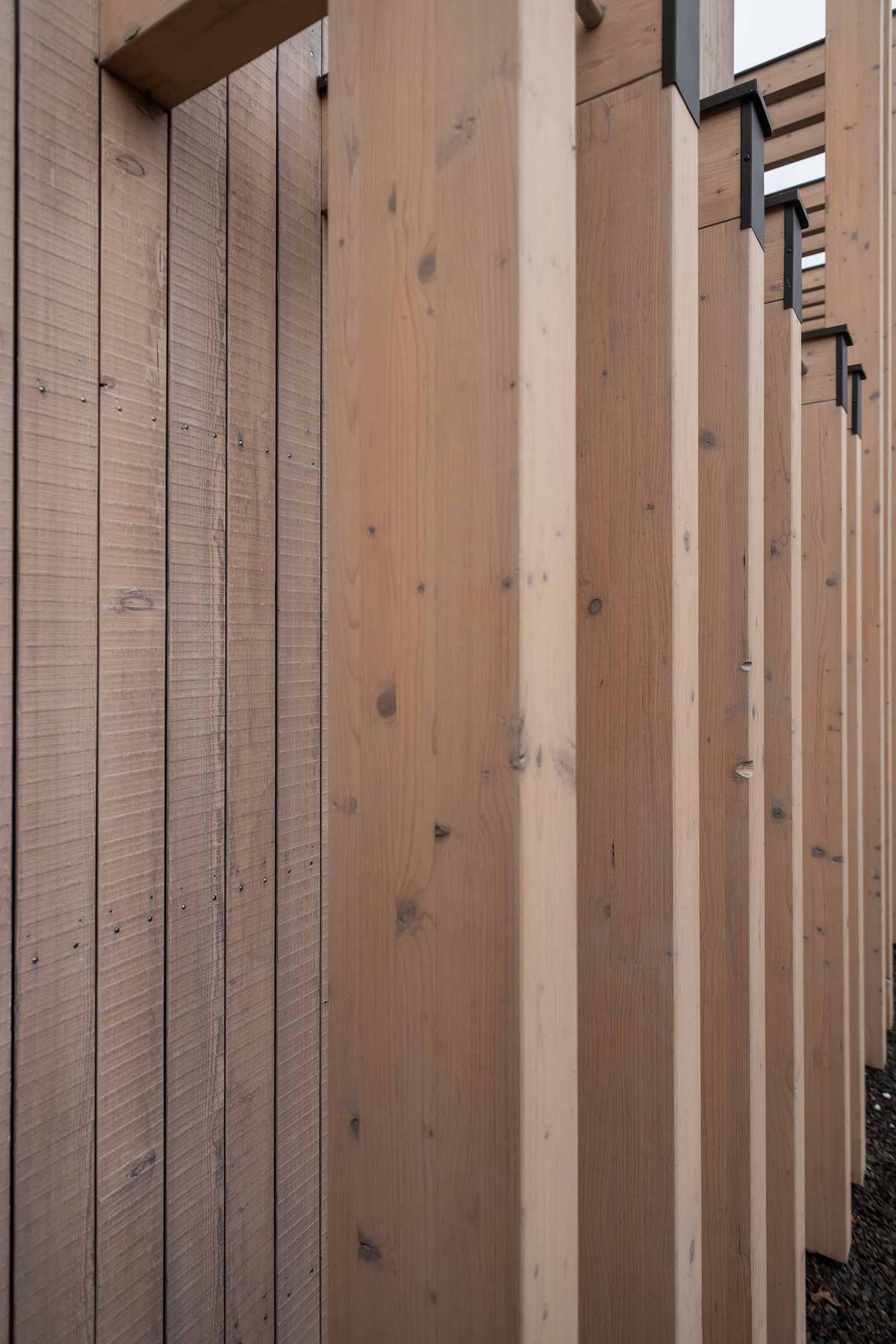 Nahaufnahme einer modernen Holzfassade mit senkrechten Elementen aus Mareiner Piz Nair, vorvergraut und im charakteristischen Bandsägeschnitt. Die Struktur des Holzes ist klar erkennbar, dazwischen Schattenfugen und dezente Befestigungspunkte.