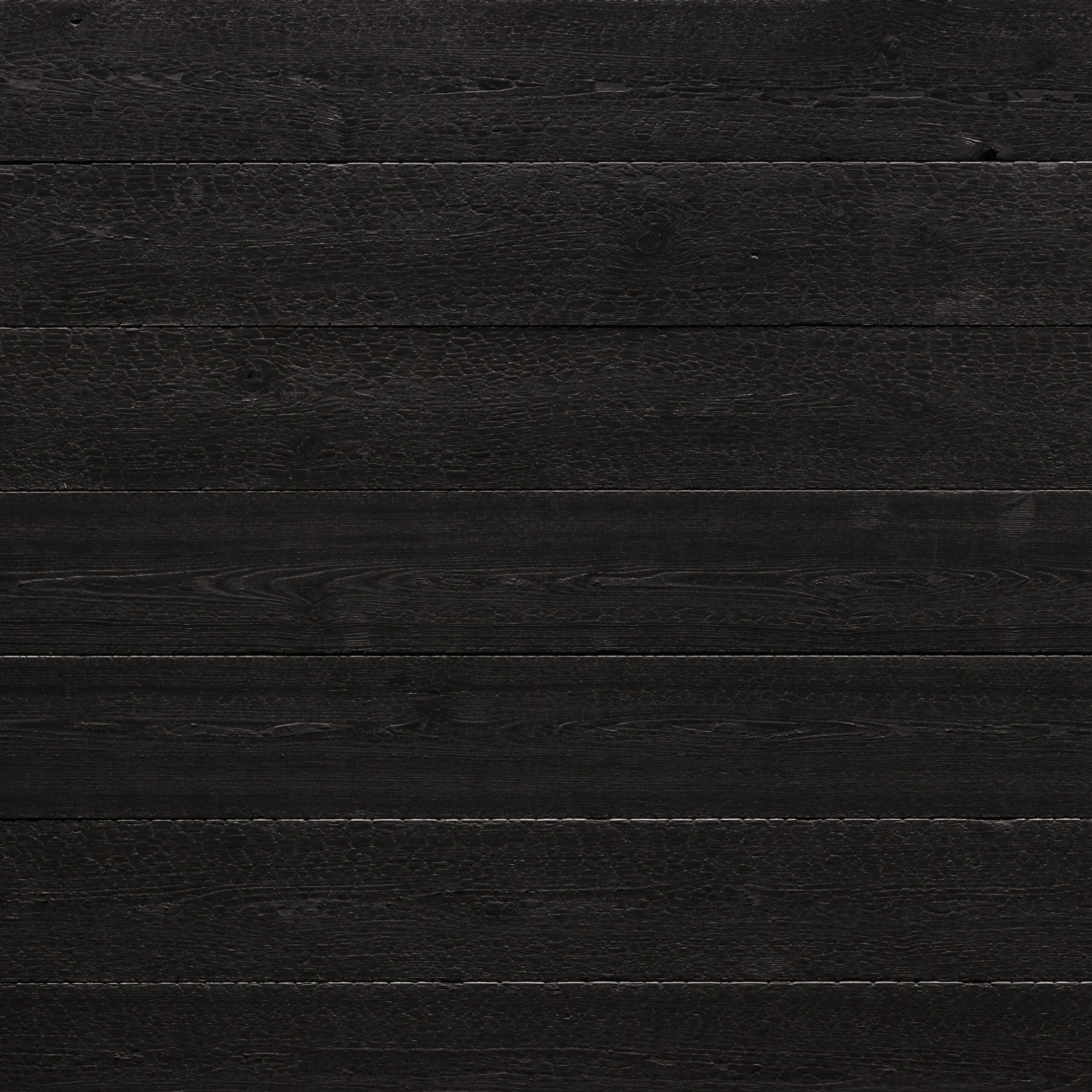 Detailansicht einer tiefschwarzen Holzoberfläche aus der Mareiner Black Edition Vulcano. Die Struktur zeigt typische Verkohlungsmuster in Schuppenoptik, die anschließend fixiert wurden. Die Oberfläche wirkt edel, archaisch und modern zugleich.